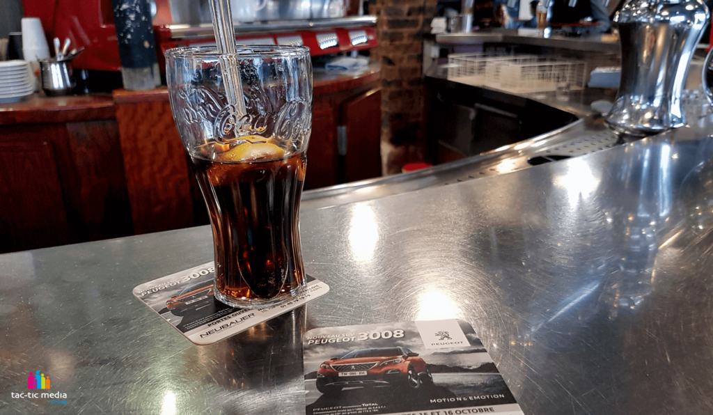 Verre de coca posé sur un sous bock publicitaire Peugeot