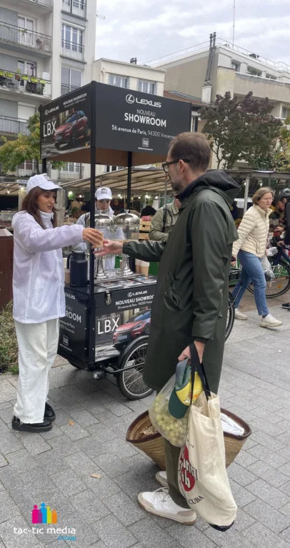 ambassadrice de marque qui distribue une boisson lors d'une activation de street marketing avec un triporteur